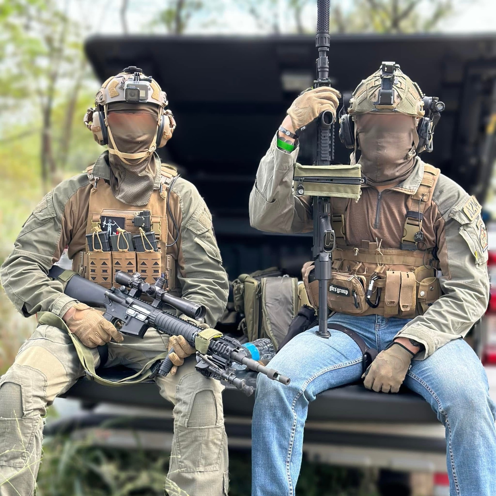 Two airsoft players in field gear seated near a vehicle.